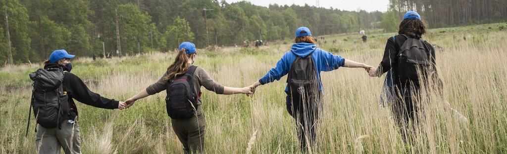 Vier Aktivist:innen laufen Hand in Hand über eine Wiese. / Aktionstage gegen Tesla in Grünheide, Brandenburg, 10. Mai 2024  Umbruch Bildarchiv © Tim Wagner