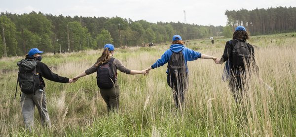 Vier Aktivist:innen laufen Hand in Hand über eine Wiese. / Aktionstage gegen Tesla in Grünheide, Brandenburg, 10. Mai 2024  Umbruch Bildarchiv © Tim Wagner